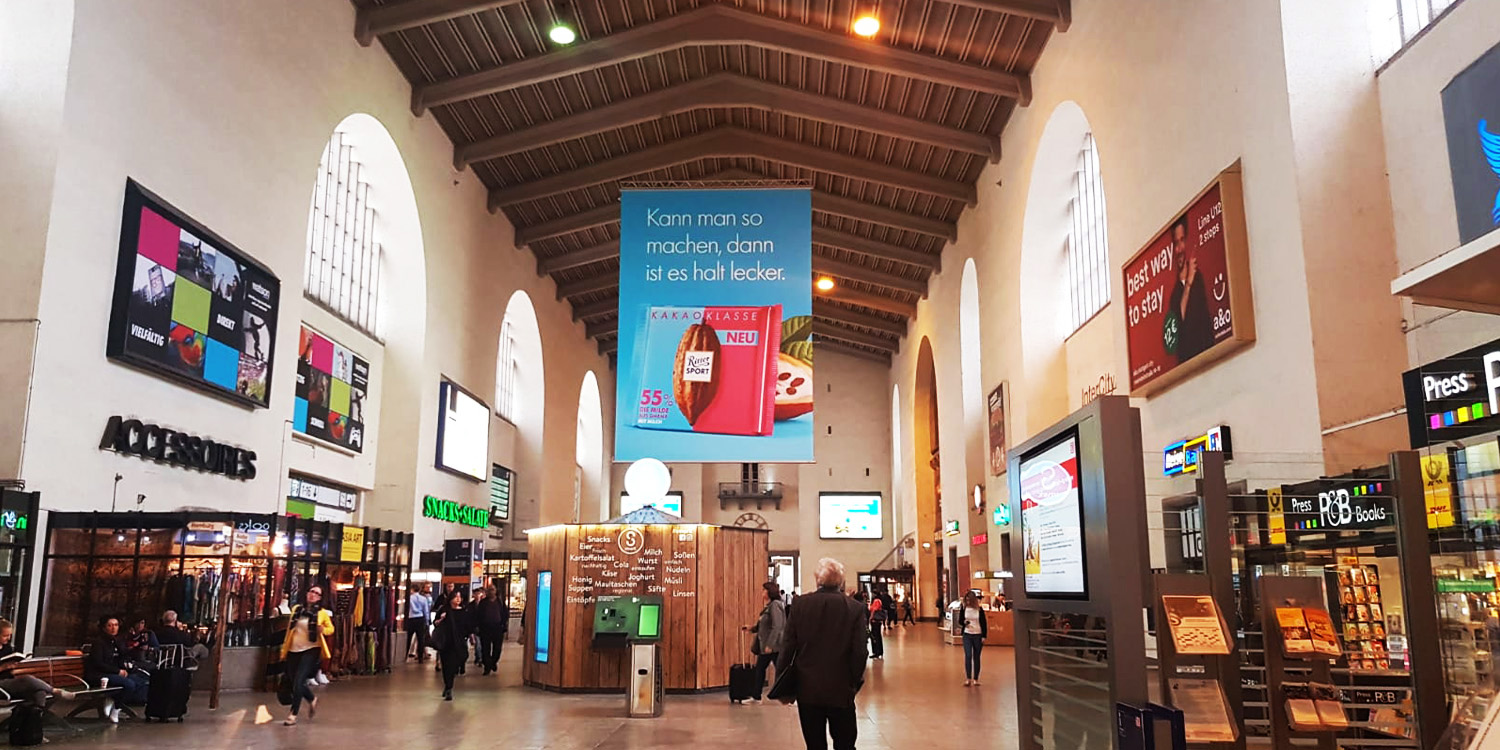 Bahnhofshalle mit Werbeanzeigen und Passanten.