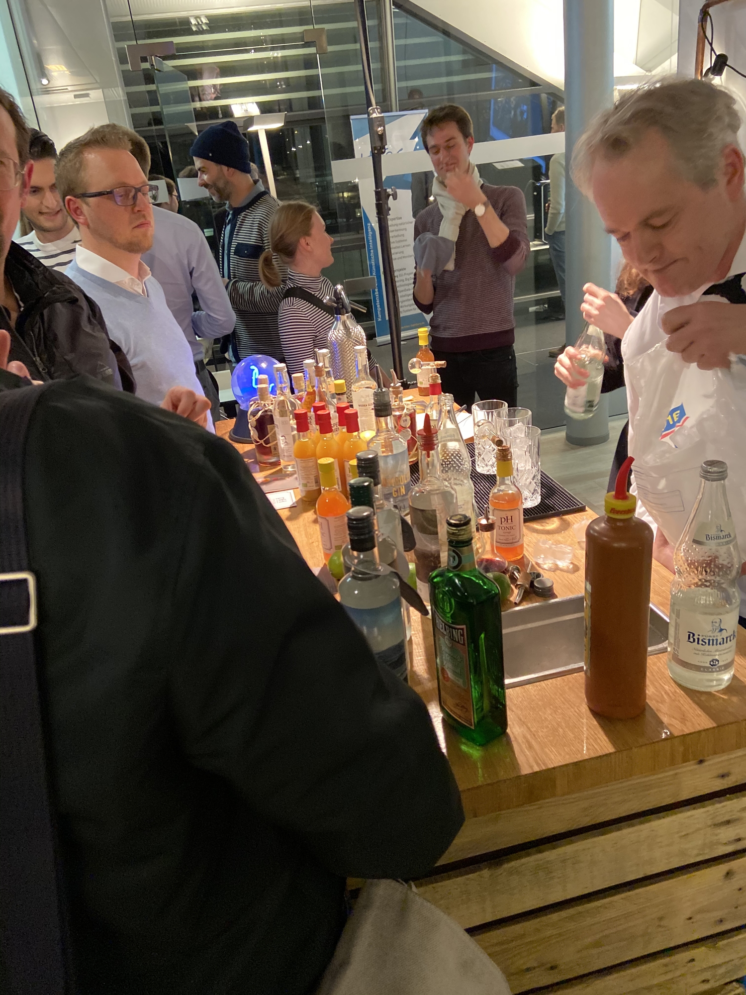 Barbereich mit verschiedenen Getränken, Menschen beobachten die Zubereitung.