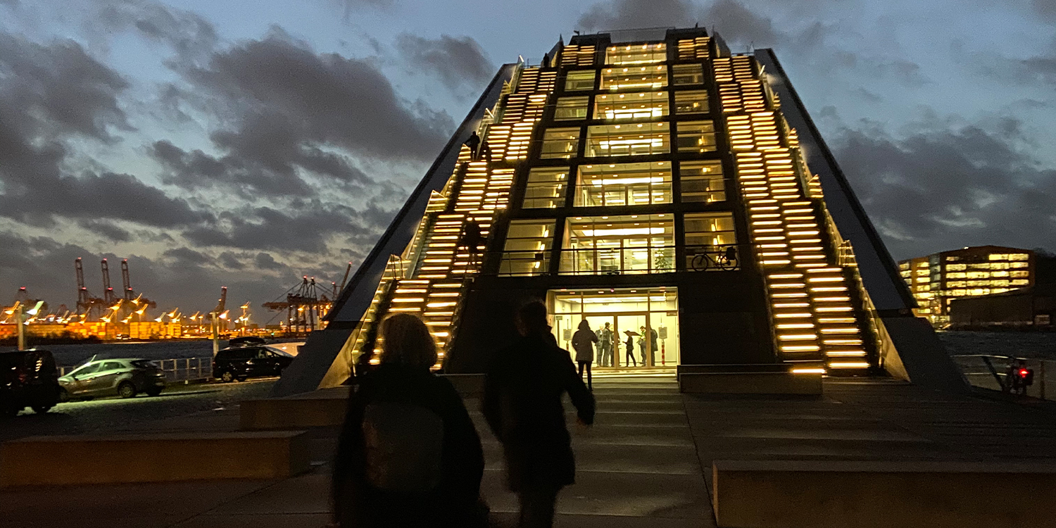 Modernes, beleuchtetes Treppengebäude bei Nacht mit Menschen davor.