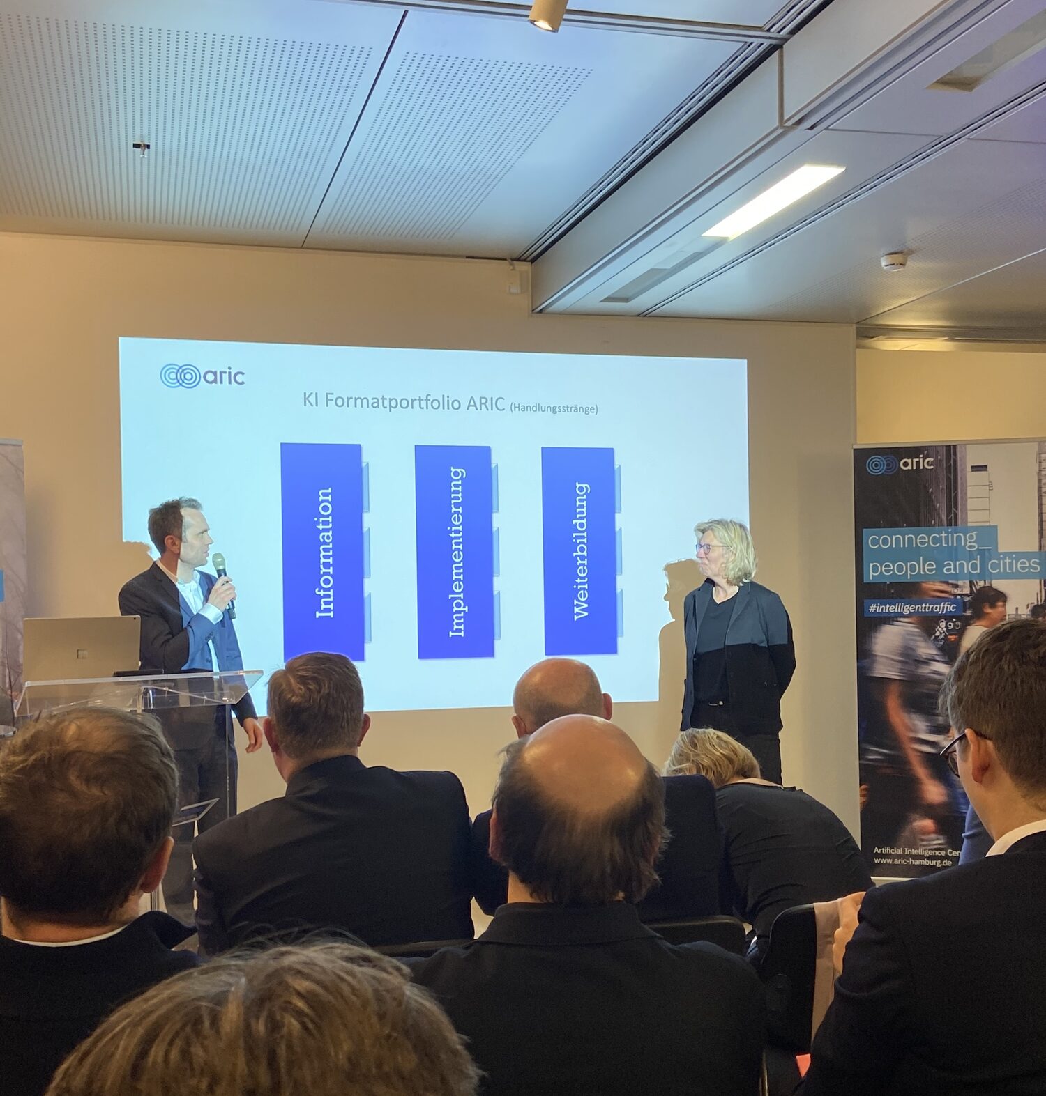 Präsentation über KI-Formatiportfolio mit zwei Vortragenden vor Publikum.