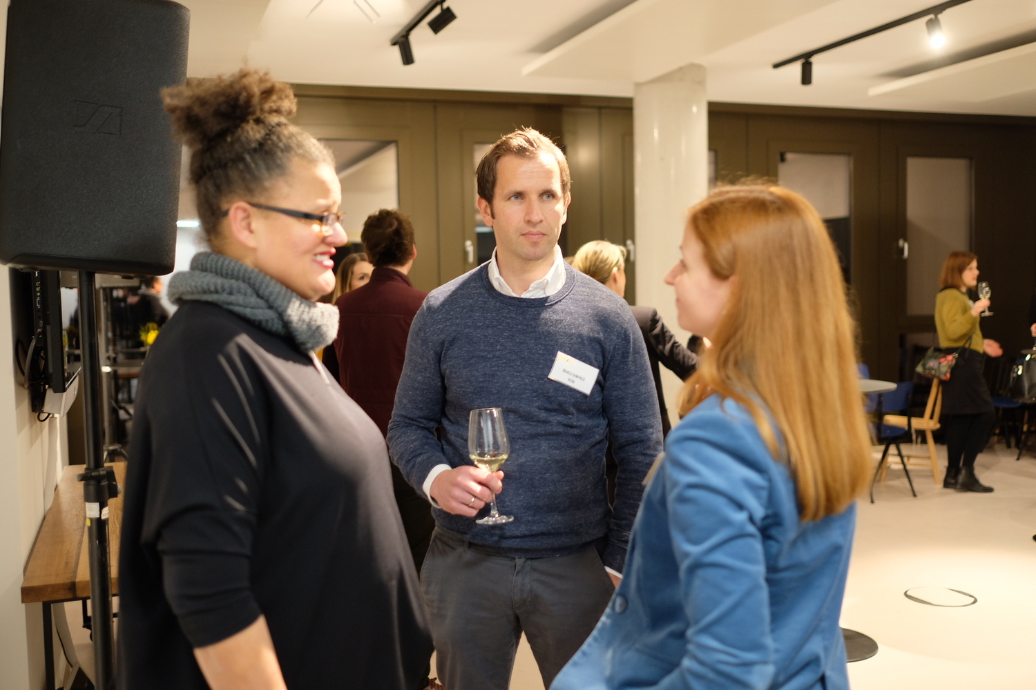 Drei Personen im Gespräch bei einem Networking-Event, einer hält ein Glas Wein.