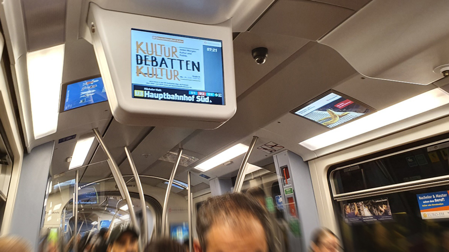 Auf Bildschirm steht Kultur Debatte in einer U-Bahn.