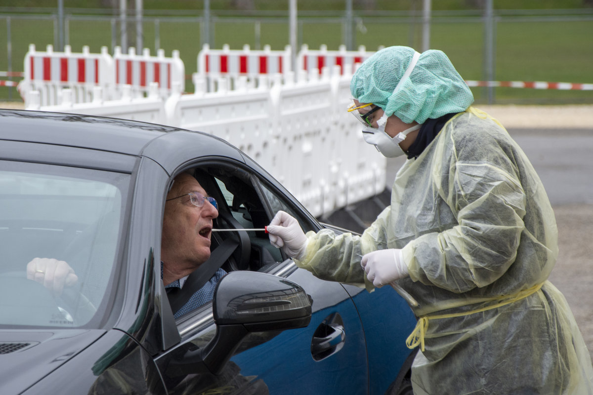 Person in Schutzkleidung nimmt einen Corona-Test an einer Teststation ab.
