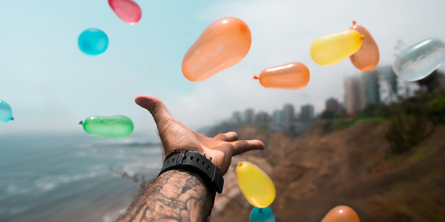 Hand wirft Ballons vor dem Hintergrund eines Strandes.