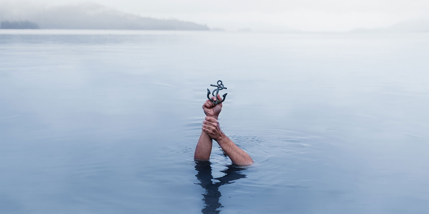 Zwei Hände ragen aus dem Wasser und halten einen Anker.