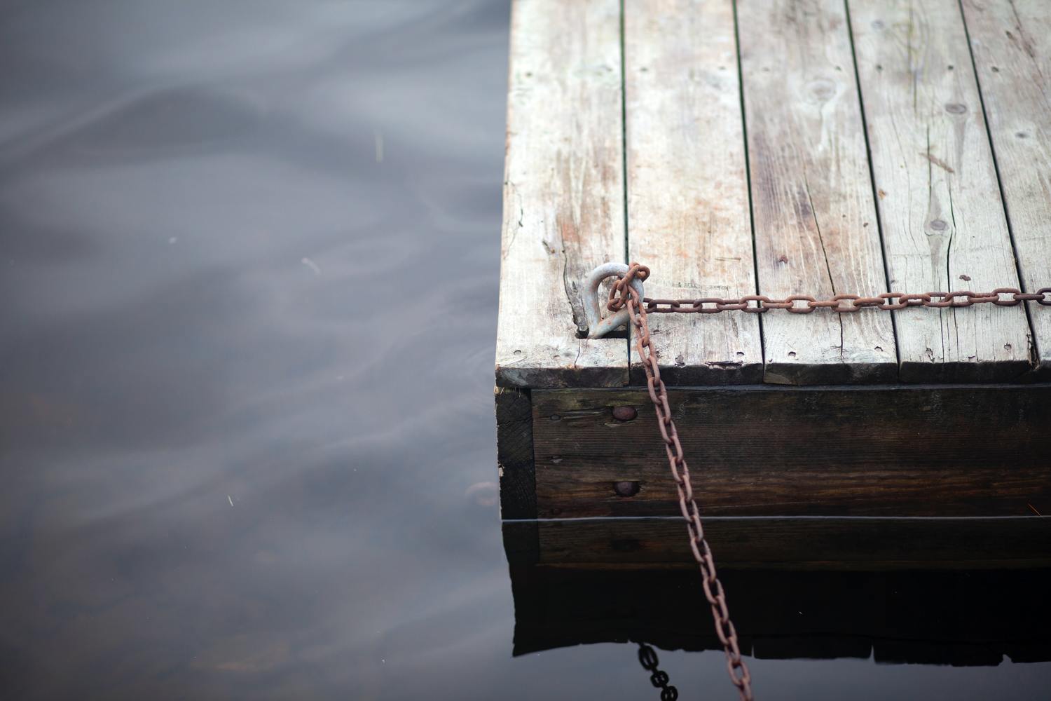 Ein hölzerner Steg mit einer rostigen Kette im Wasser.