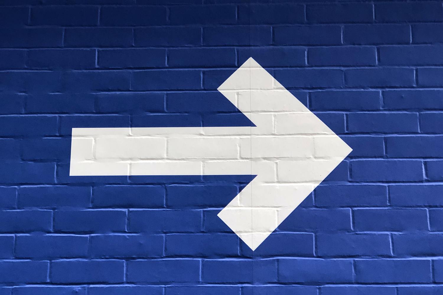 Weiße Pfeilmarkierung auf einer blauen Backsteinwand.