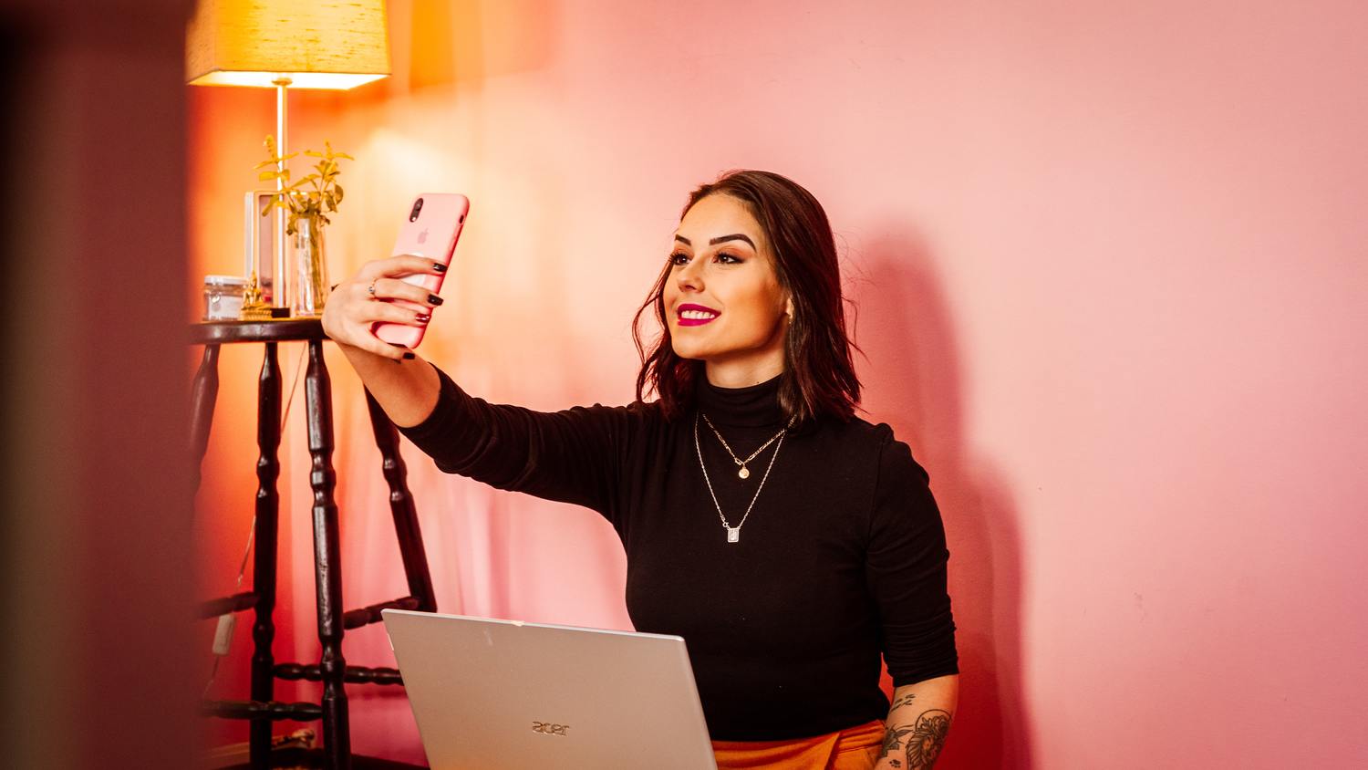 Frau macht ein Selfie mit Smartphone und Laptop.
