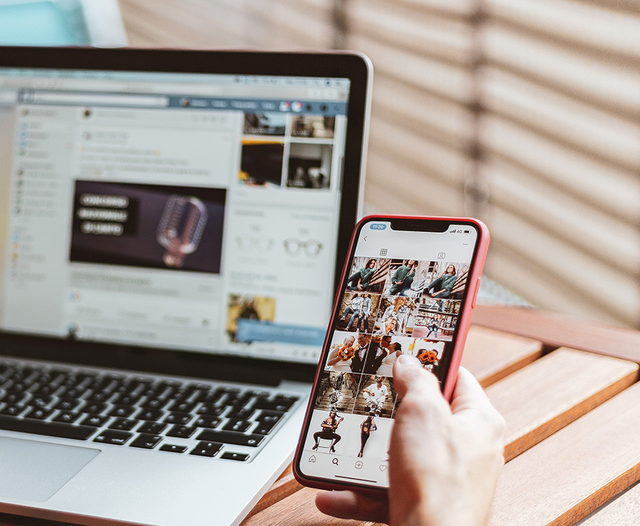 Person nutzt Smartphone, während Laptop im Hintergrund läuft.
