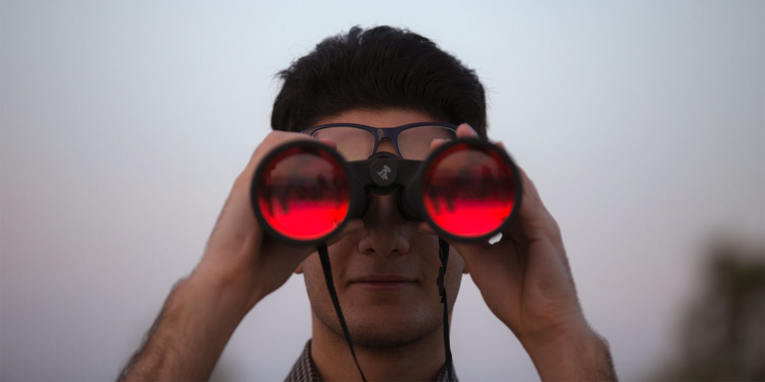 Mann schaut durch ein Fernglas mit roten Gläsern.