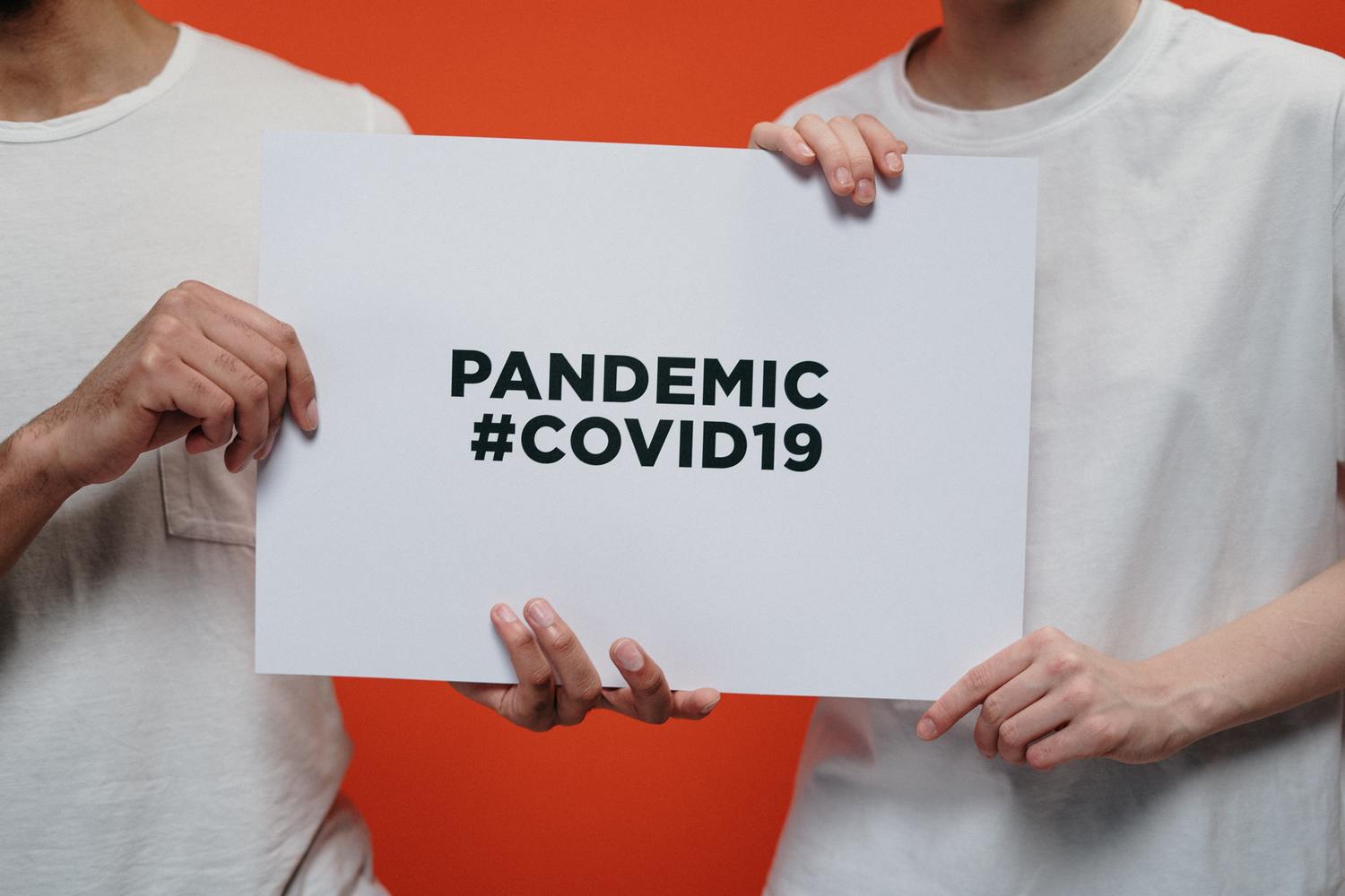Hände halten ein Schild mit der Aufschrift „PANDEMIC #COVID19“.