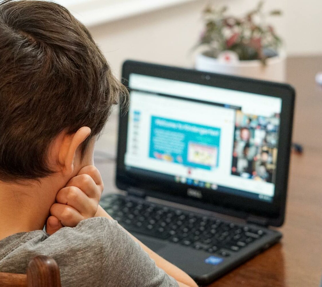 Kind sitzt vor einem Laptop und nimmt an einer Online-Lektion teil.