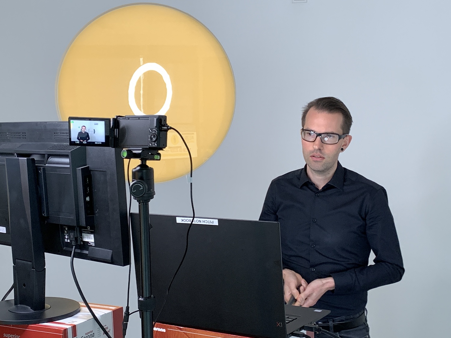 Mann sitzt vor einer Kamera mit Ringlicht bei einer Online-Präsentation.