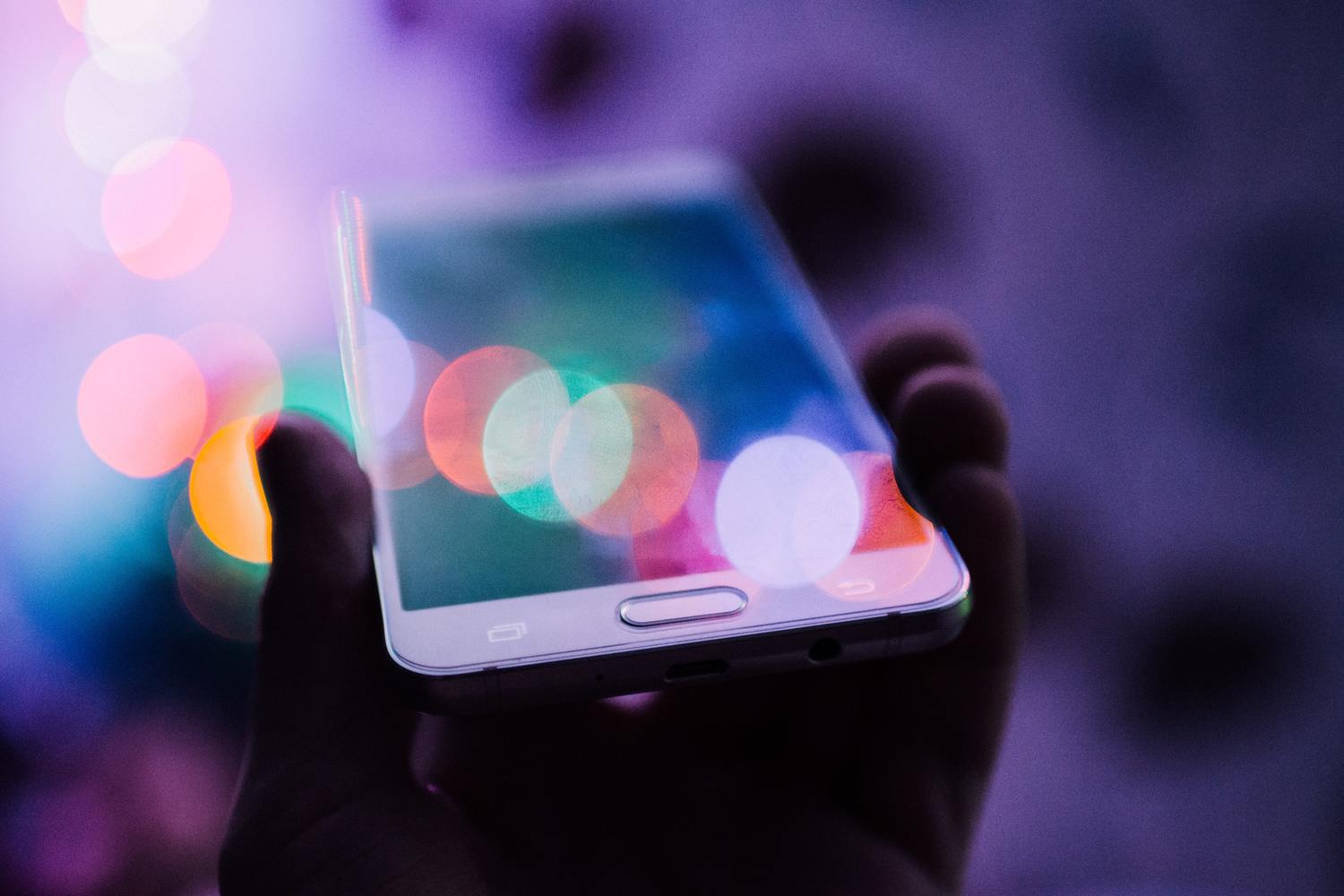 Hand hält ein Smartphone mit verschwommenen, leuchtendem Lichtern.