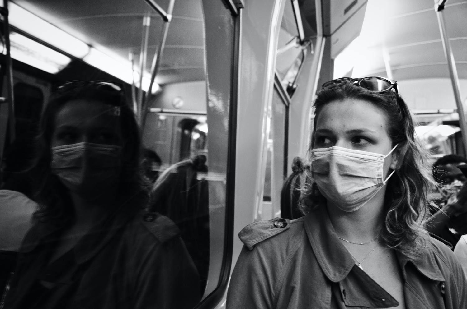 Frau mit Maske spiegelt sich in einer U-Bahn-Scheibe.