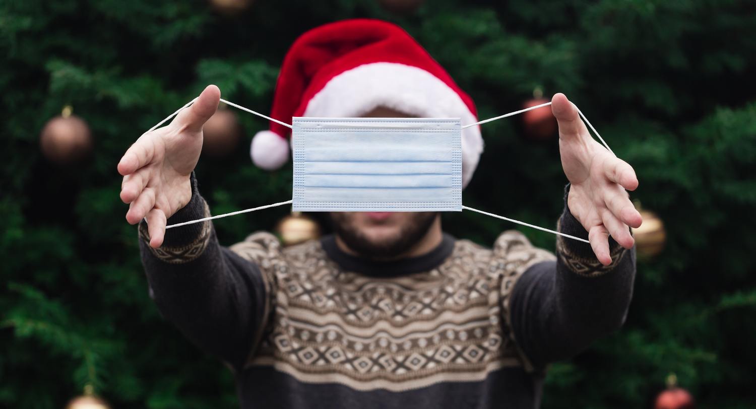 Person mit Weihnachtsmütze und Maske hält die Hände vor sich.