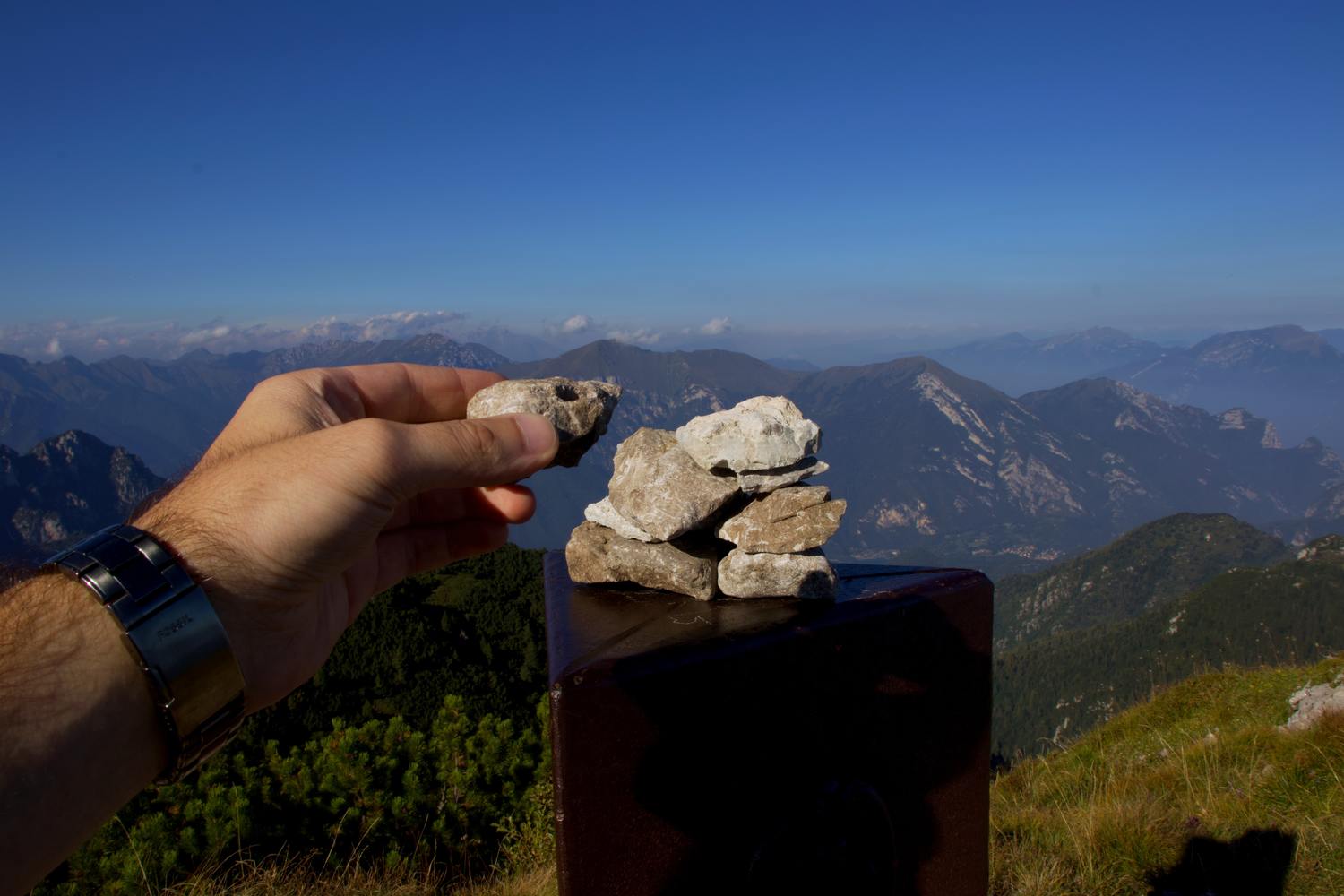 Hand hält kleine Steintürme mit Berglandschaft im Hintergrund.
