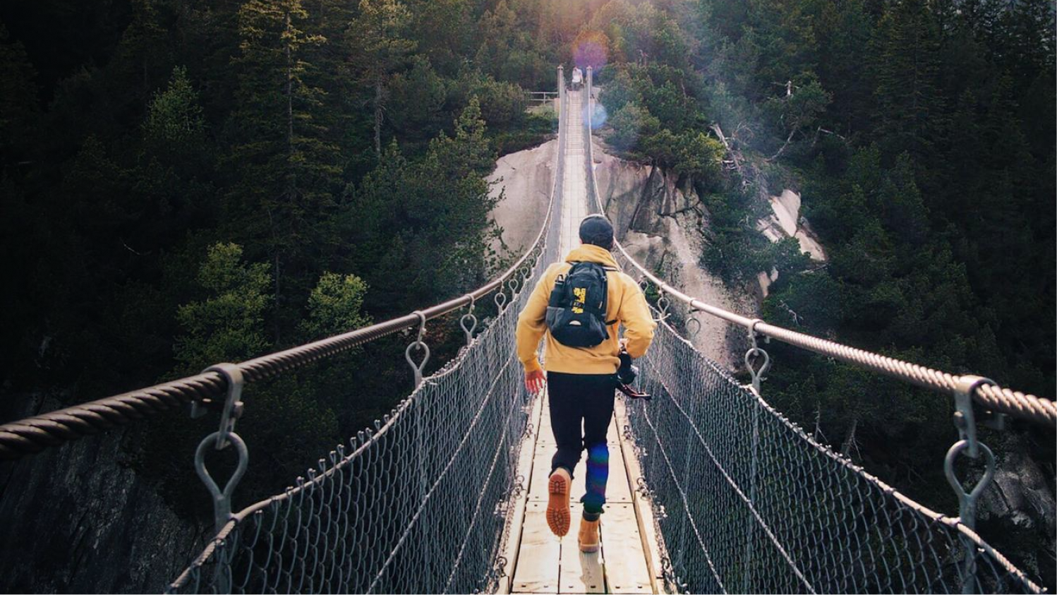 Pilot Referenz Jack Wolfskin Desktop Mann läuft in atemberaubender Landschaftskulisse über eine Hängebrücke
