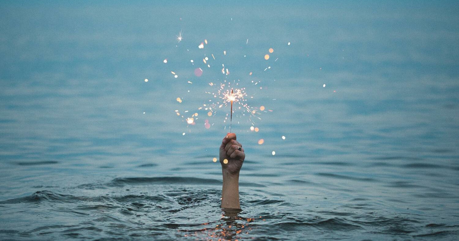 Hand ragt aus dem Wasser mit Funken.