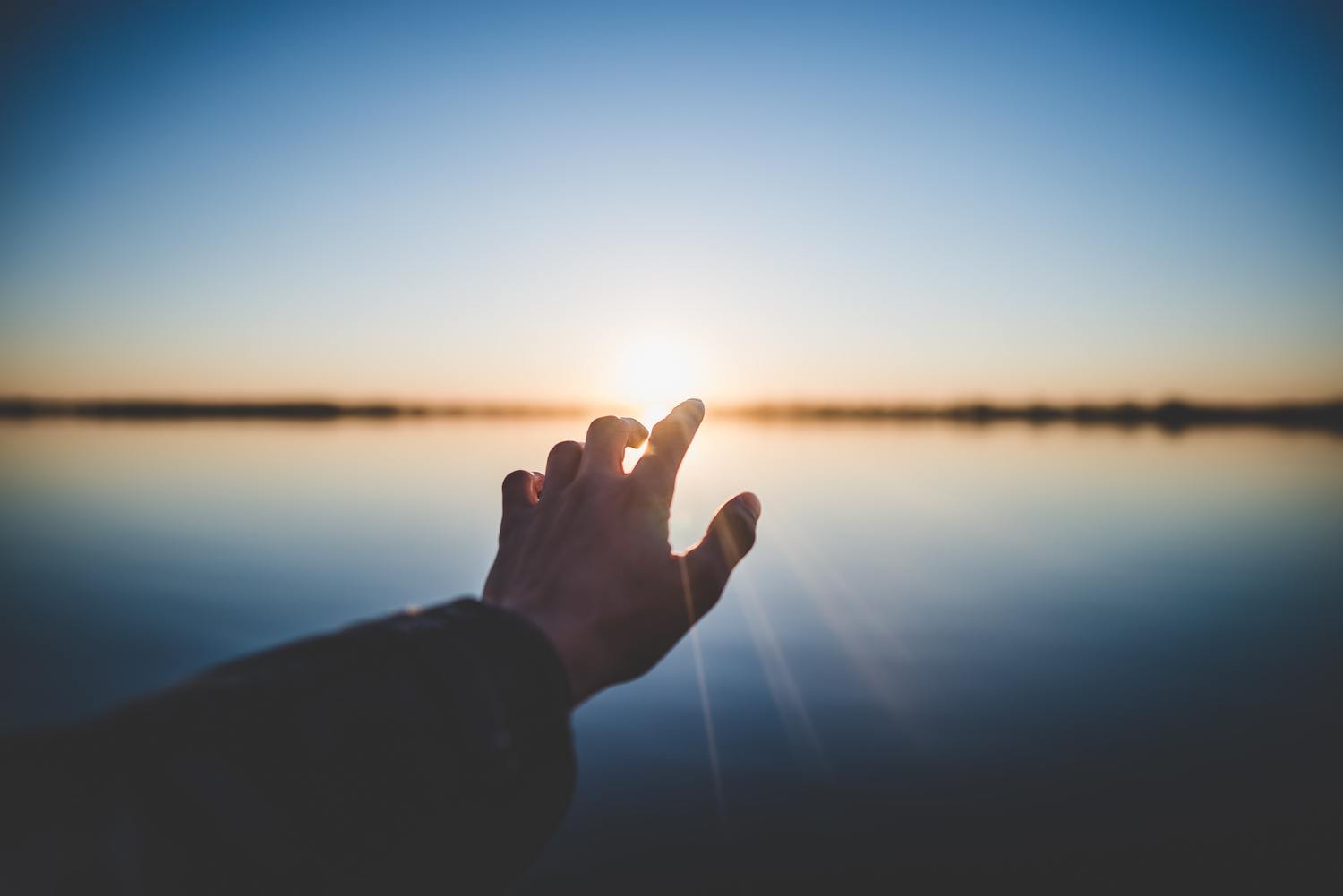 Hand zeigt zur Sonne über Wasser.