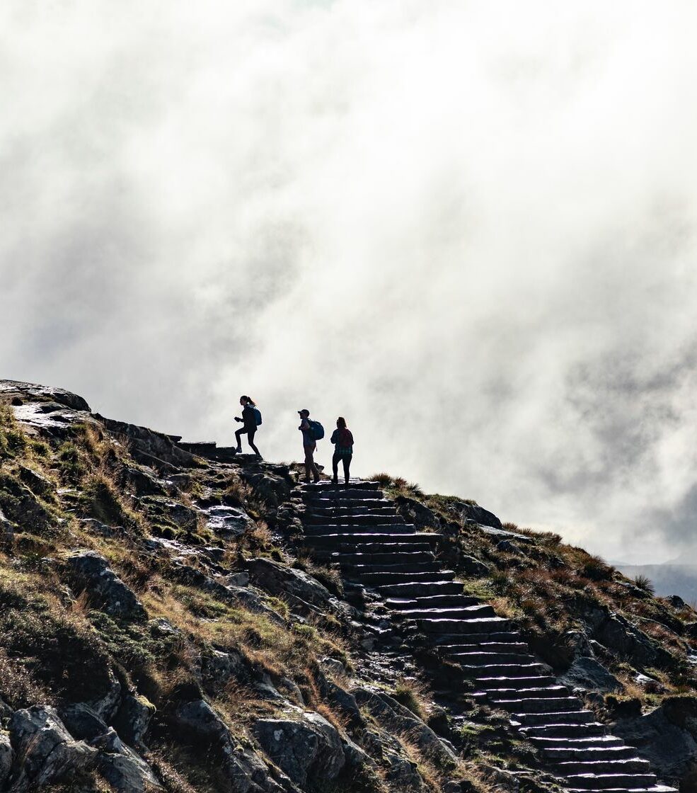 Silhouetten von Menschen, die eine steile Treppe auf einem nebligen Bergpfad hinaufsteigen.
