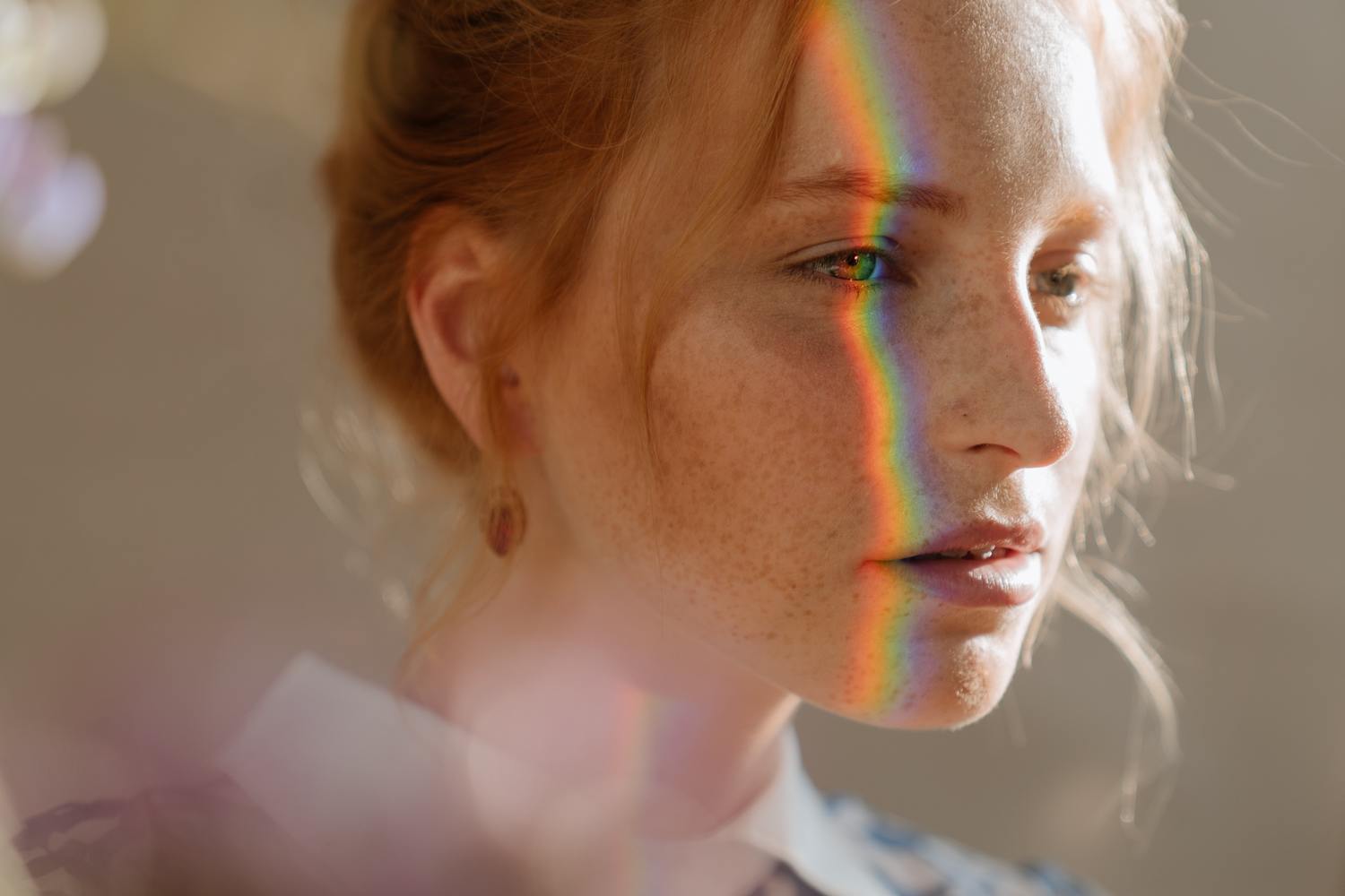 Eine Frau, deren eine Gesichtshälfte die Spiegelung eines Regenbogens zeigt.