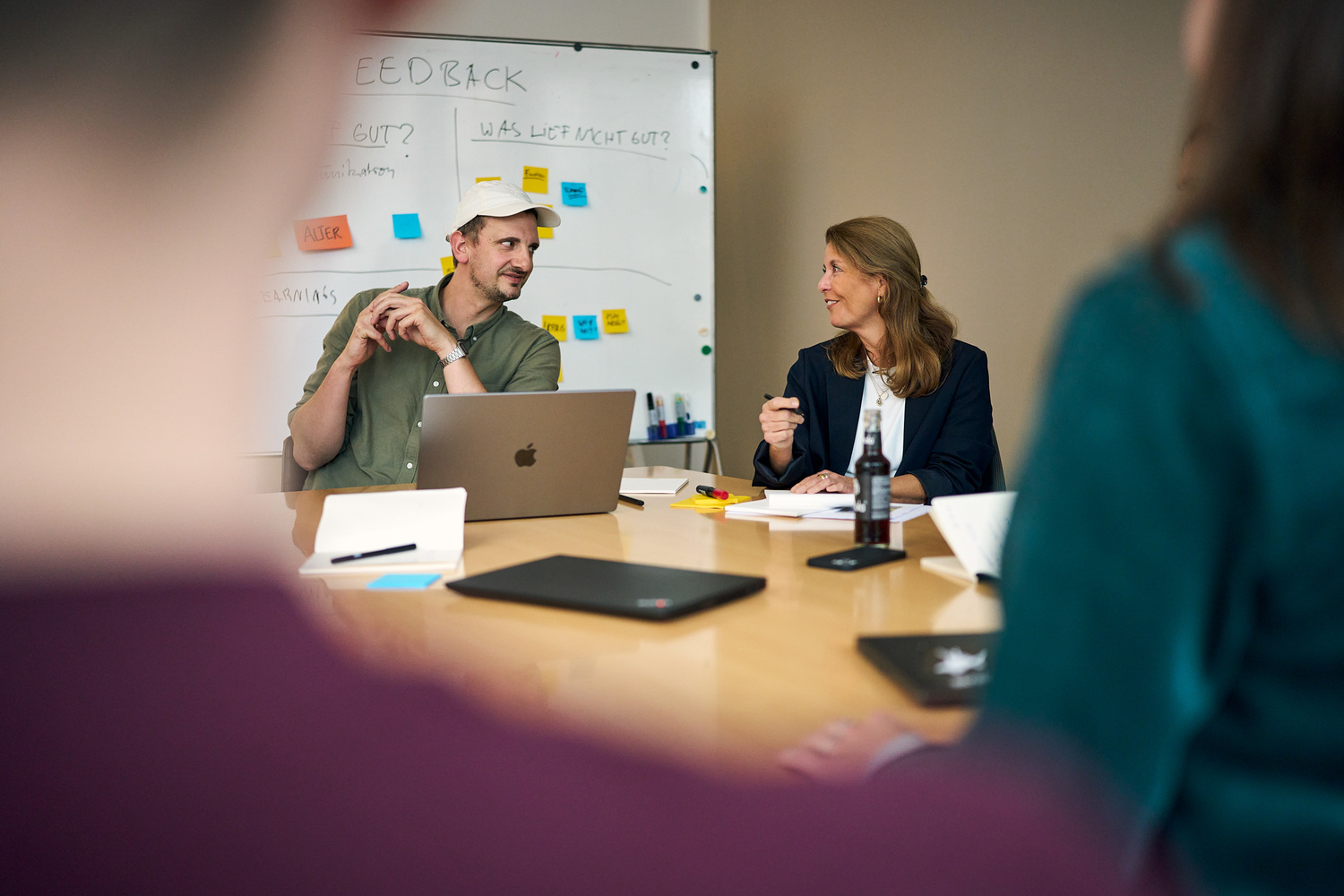 Eine Gruppe von Personen sitzt um einen Tisch mit einem Laptop und diskutiert gemeinsam.