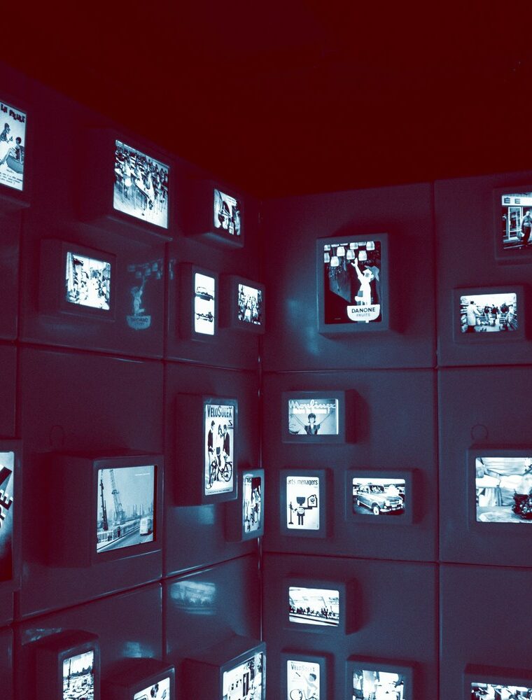 Eine dunkle Galerie- oder Ausstellungswand, auf der viele kleine beleuchtete Bildschirme angebracht sind.
