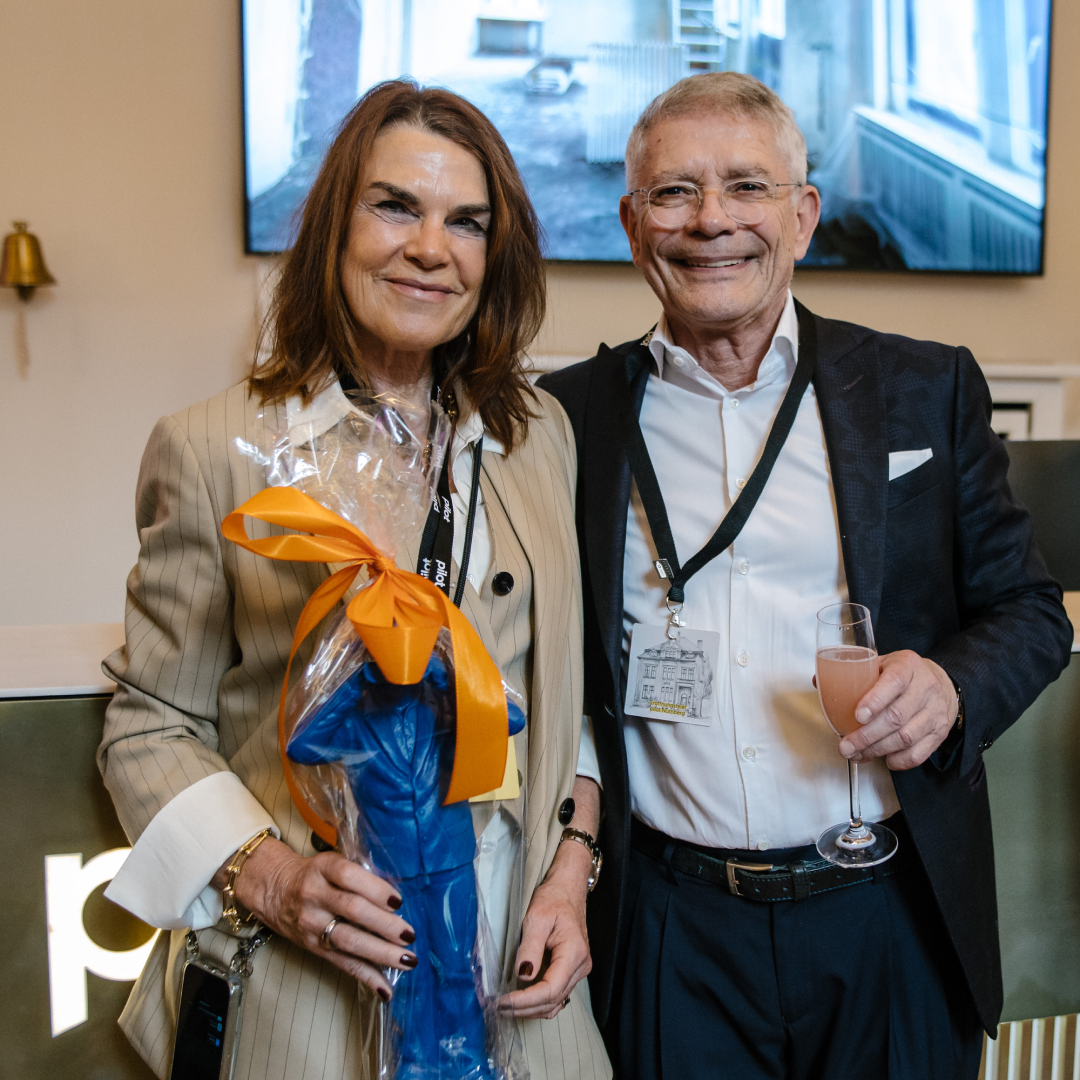 Eine Frau und ein Mann lächeln und halten jeweils eine Trophäe und ein Getränk.