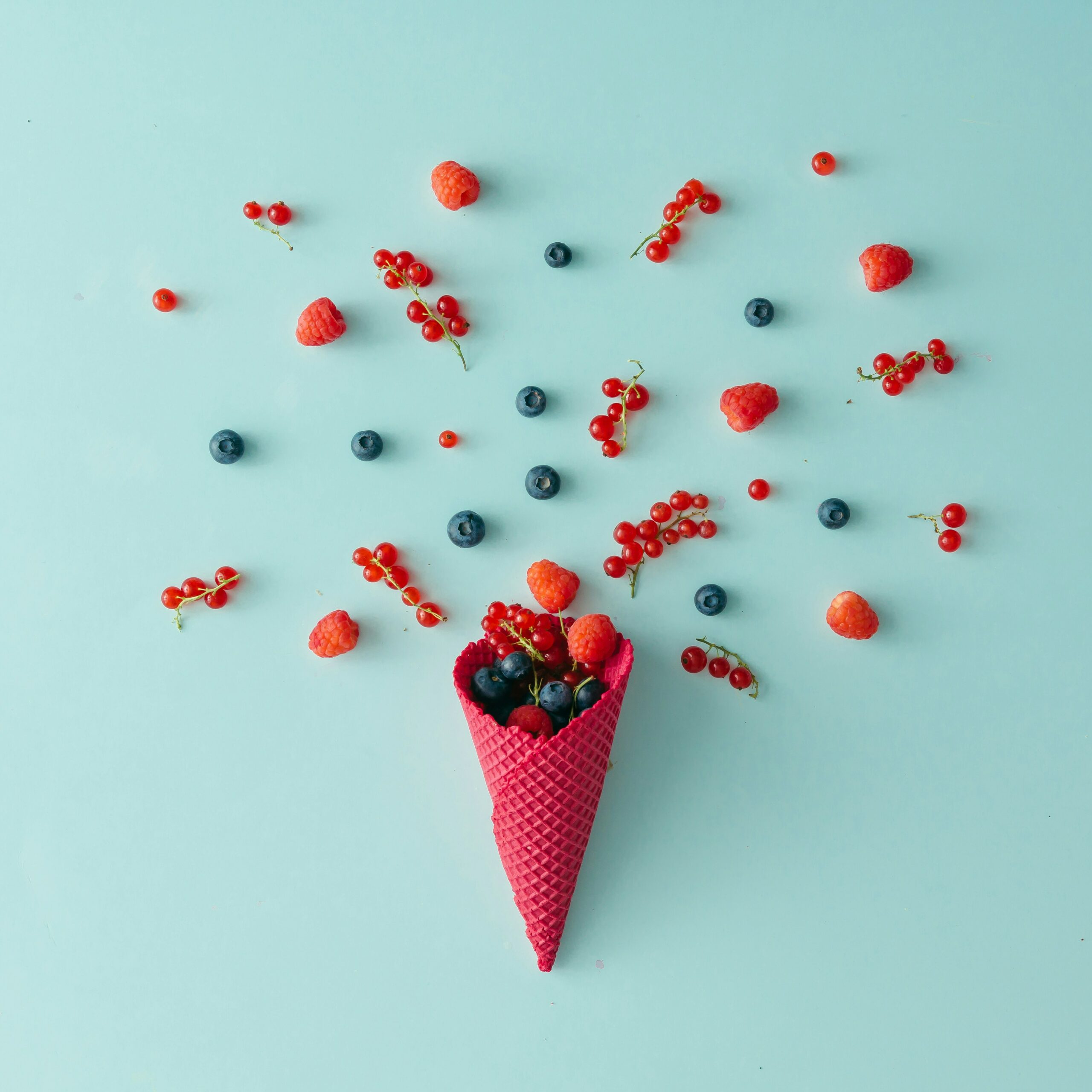 Getty Images S03u5Bm3A2E Unsplash Scaled Pinke Eiswaffel auf hellblauem Grund aus dem rote Früchte fliegen
