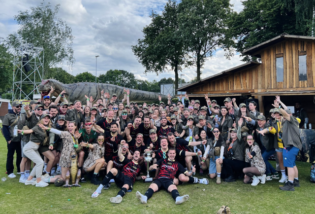 Eine große Gruppe von Menschen hat sich beim Football Agency Cup 2024 für ein Gruppenbild vor der pilot Hütte aufgestellt. Alle tragen Kostüme oder Fußballtrikots.