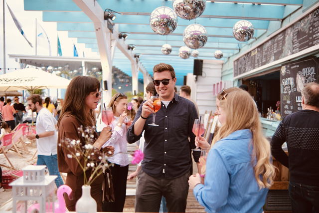 Drei Menschen stoßen mit Getränken an bei der Sommerparty von pilot Hamburg im Beachclub.