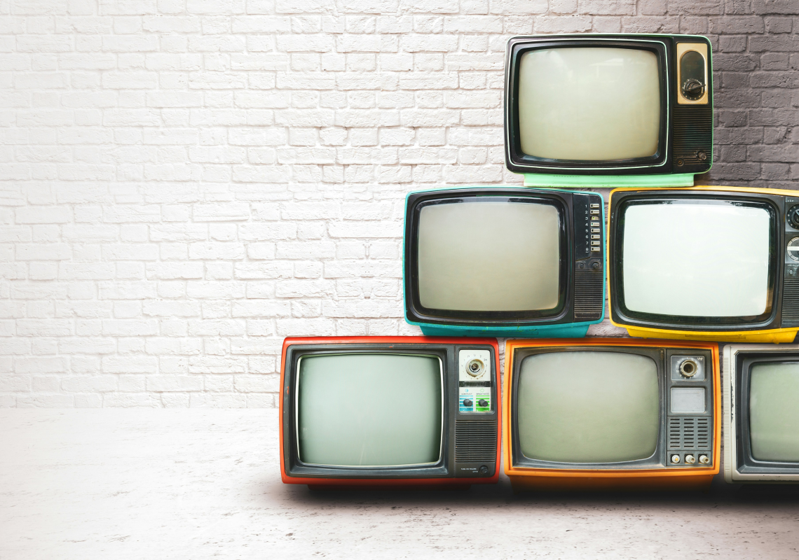 Bunte, gestapelte, alte Röhrenfernsehr vor einer grauen gemauerten Wand