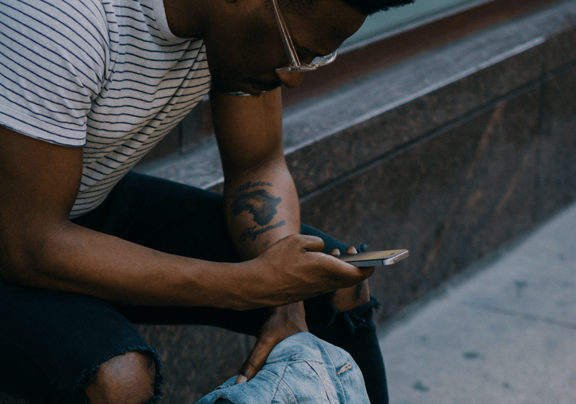 Junger Mann sitzt auf Treppenstufe und schaut auf sein Handy