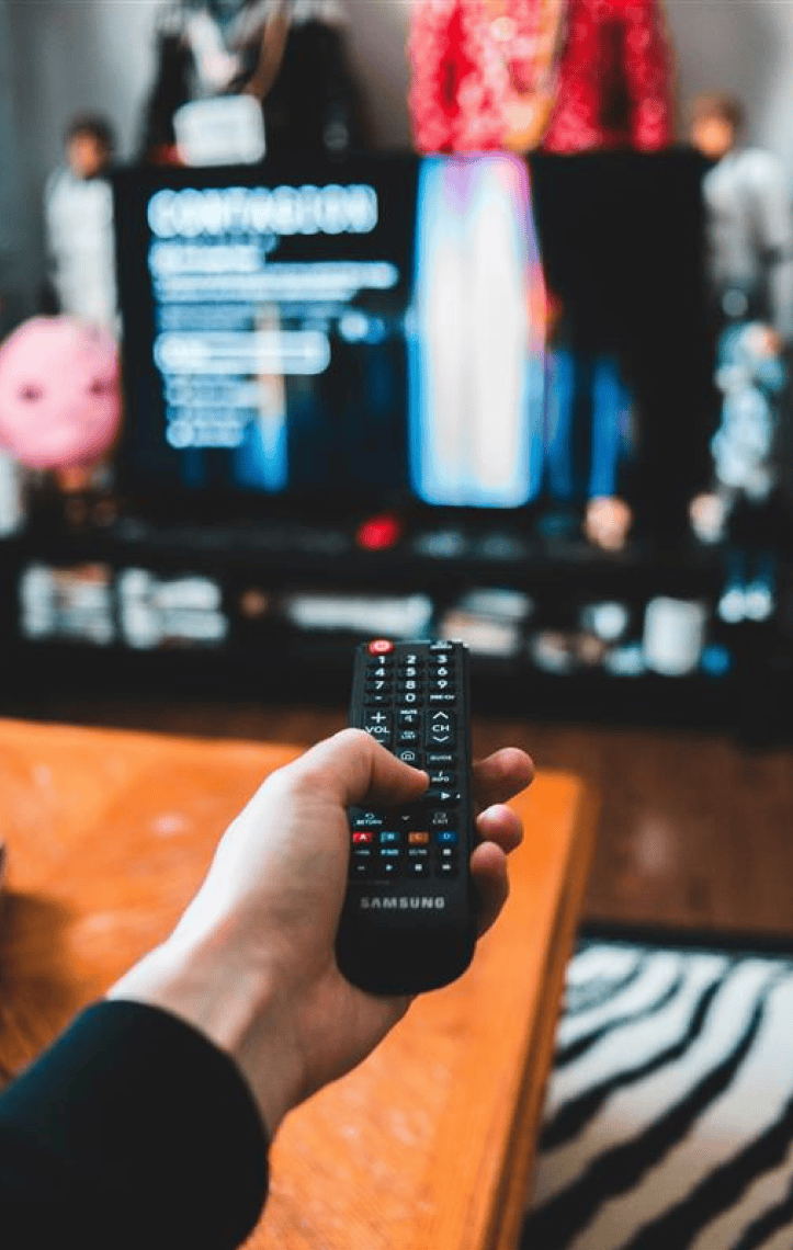 Eine Hand hält eine Fernbedienung und schaltet auf einem Fernseher Netflix ein.